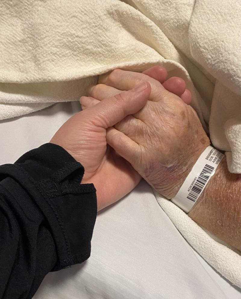 Two people holding hands, one an elderly person with hospital band around wrist
