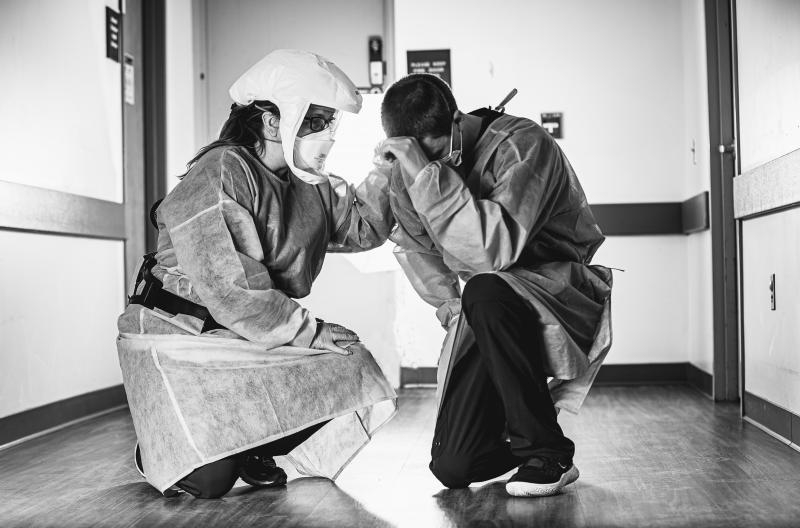 Two medical workers kneeling in hallway, one appears to be comforting the other