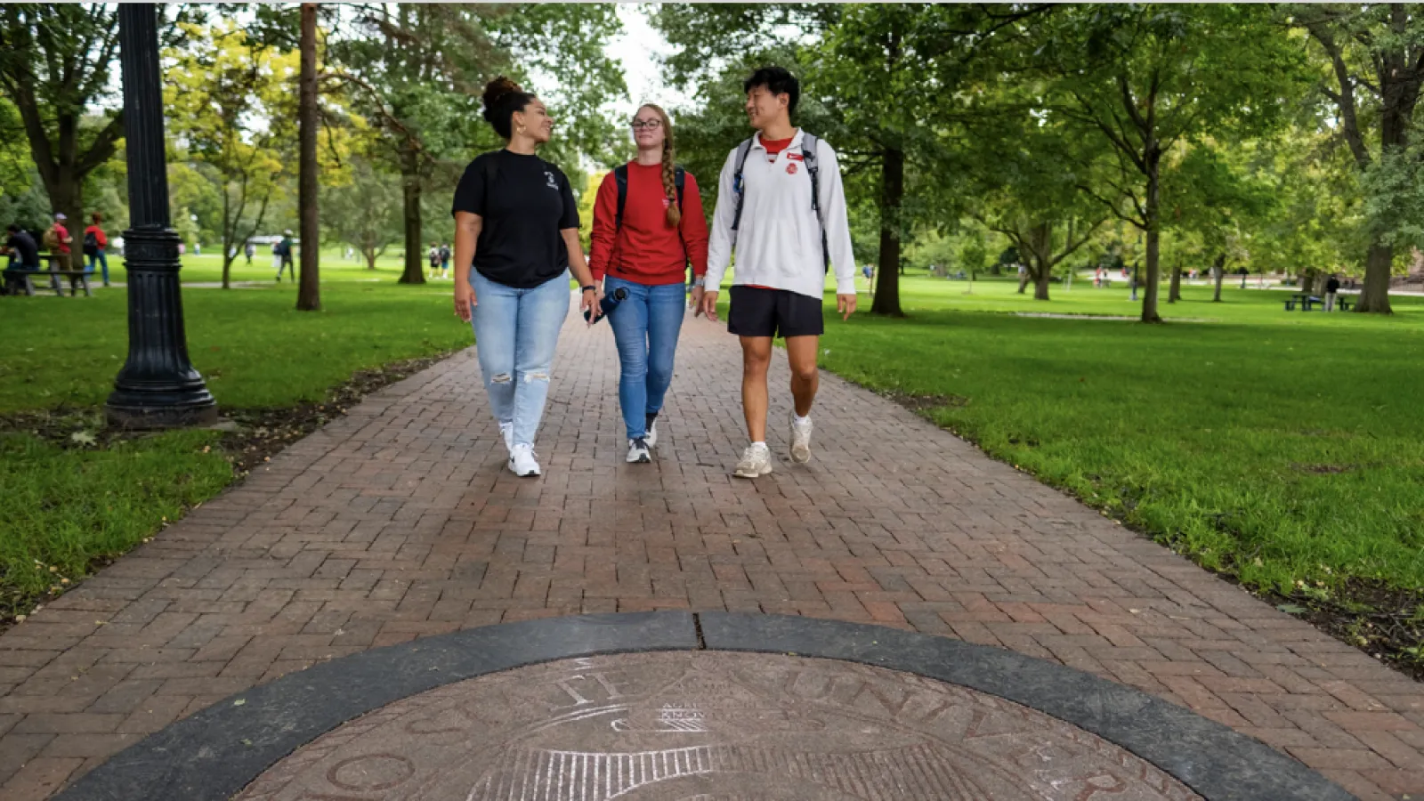 Three students walking toward the camera on The Oval.