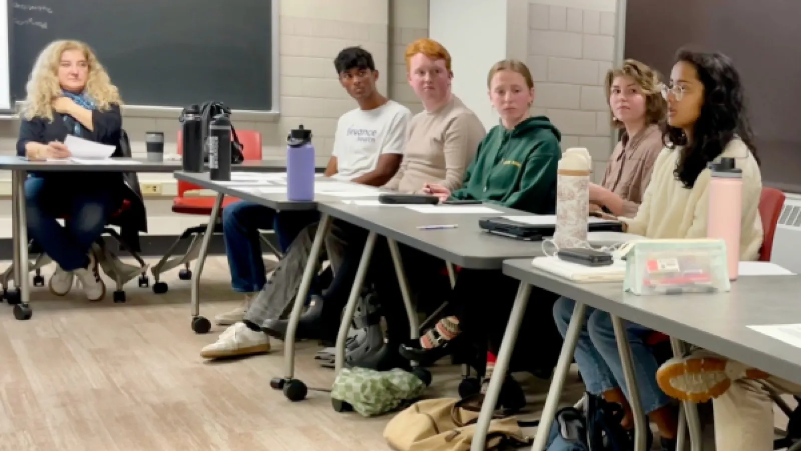 Five students seated in a line listening to one student speak