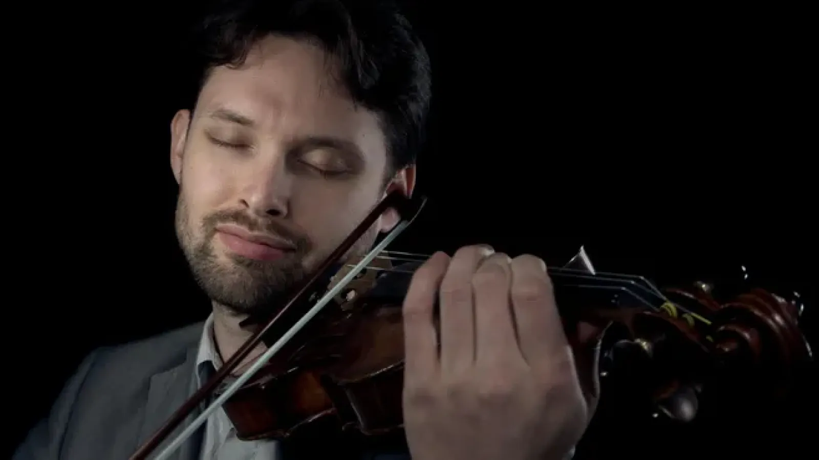 A close-up photo of Aaron Yarmel playing the violin with his eyes peacefully closed